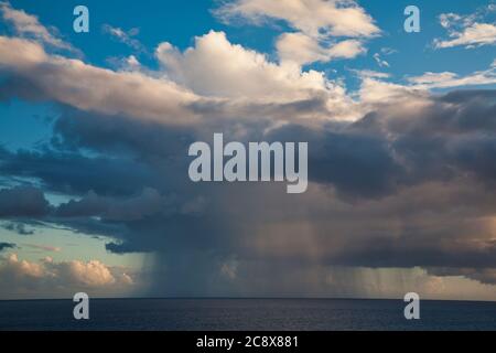 A distant view of a rainstorm over the Caribbean sea with local rain clouds above set in an otherwise blue sky, view includes the horizon Stock Photo