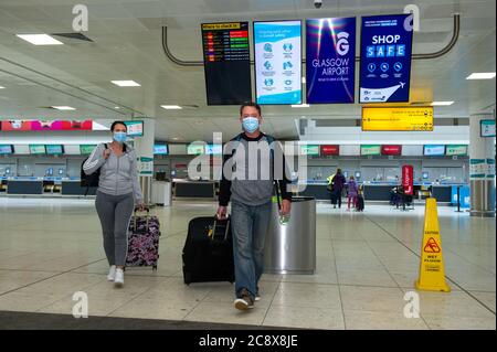 Glasgow, Scotland, UK. 27th July, 2020. Pictured: Passengers wearing blue surgical face masks seen wheeling their luggage in the airport terminal. Inside Glasgow Airport's terminal 1. The Scottish Government announced as from 00:01 this morning that all incoming flights from Spain into Scotland would need a period of 14 days quarantine. Jet2 Airlines have operated a number of flights this morning and a further afternoon service to Tenerife despite the new travel restrictions. Credit: Colin Fisher/Alamy Live News Stock Photo