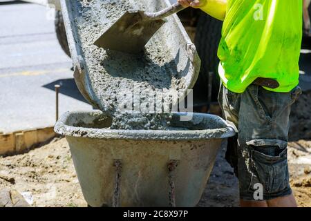 Wheelbarrow with shovel full of cement concrete of concrete mixer truck in industrial worker Stock Photo