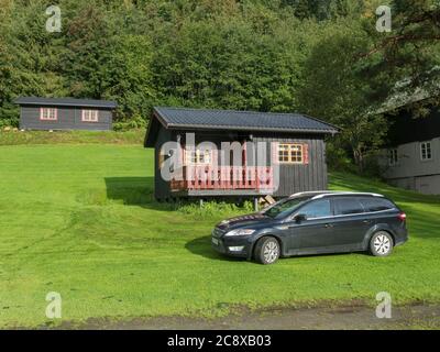 Storen, Norway, September 7, 2019: View of Classical Norwegian Camping site with traditional wooden cabins, lush green grass and trees. Black car Stock Photo
