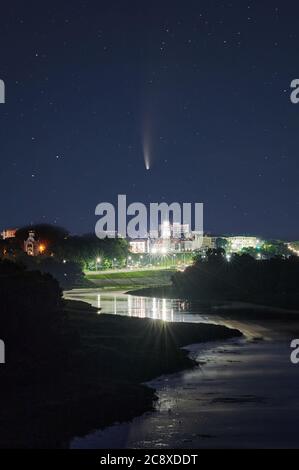 Comet neowise in starry night sky over bright city Stock Photo