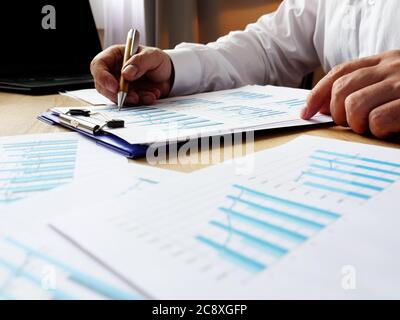 A man in a white shirt checks financial charts and tables at the table. Paperwork and reporting. Stock Photo