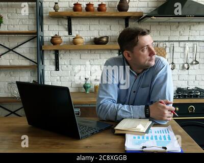 A man sits in the kitchen and works remotely. Stock Photo