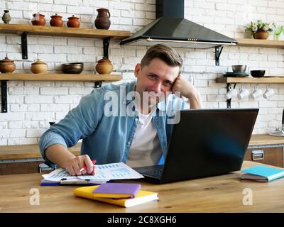 Freelancer works remotely from home. A man with a laptop in the kitchen. Stock Photo
