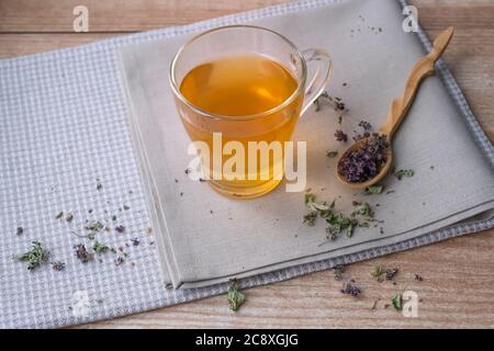 Warm oregano tea on beige linen napkins on the table. Wooden small spoon with dry flowers and leaves of oregano. Copyspace Stock Photo