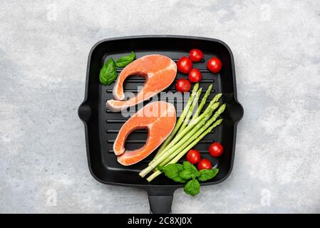 Salmon steaks with asparagus, tomatoes and basil on a pan. Isolated on grey concrete background. Healthy food Stock Photo