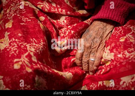 Close up details of the wrinkle hand of a elder Nepalese woman wearing a red traditional dress. Nepal Asia Stock Photo