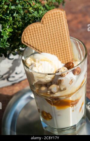 Ice cream in a glass with nuts, caramel sauce, cream and waffle, outdoor Stock Photo