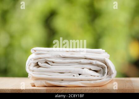 A stack of folded white bedding. Bed sheet set on blurred foliage background. Stock Photo