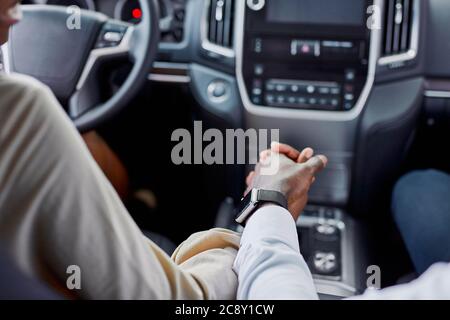 lovely black couple holds each other's hand while sitting inside of car. in dealership Stock Photo