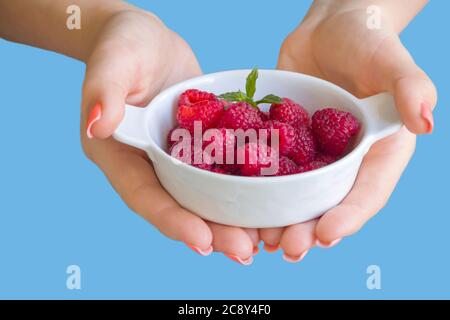 White small bowl with fresh raspberries in hands, blue background Stock Photo