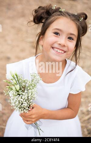 a child girl holds a bouquet of white flowers on a blurry background.dark hair , white flowers in her hands, white dress Stock Photo