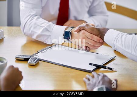 young caucasian dealer giving key to new african american owner and shaking hands in auto show or salon. auto business, car sale, deal, gesture and pe Stock Photo