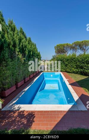 A swimming pool with blue coating in a private garden is completely empty, waiting to be filled with water for the start of the summer season Stock Photo