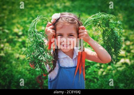 Beautiful little child with carrots in garden. Girl farmer, horticulture. Stock Photo
