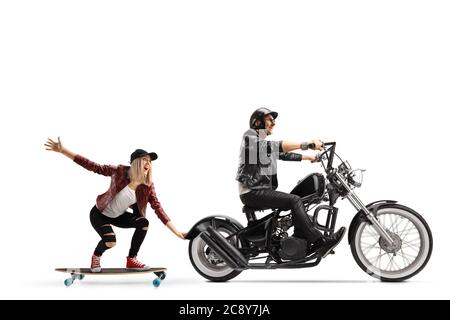 Full length profile shot of a biker on a chopper pulling a young woman on a skateboard isolated on white background Stock Photo