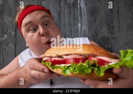 overweight caucasian man can not adhere to a healthy lifestyle and diet, doing sport exercises and at the same time eat unhealthy food Stock Photo