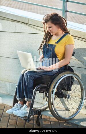 serious disabled girl looking for a job in the internet,reading e-book,doing shopping online . full length side view photo. Stock Photo