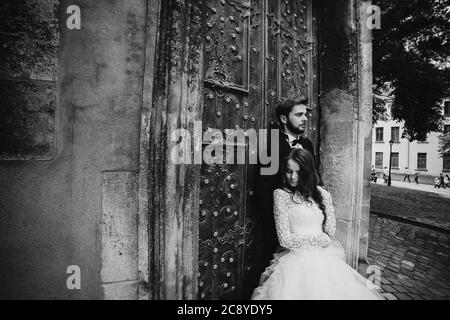 black and white photo. Wedding couple hugs near the vintage green door. Stone walls in ancient town background. bride with long hair in lace dress and Stock Photo