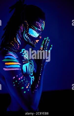 side view on calm african man with fluorescent prints on skin praying for the best, stand in the pose of prayer. luminescence, fluorescence, body art Stock Photo