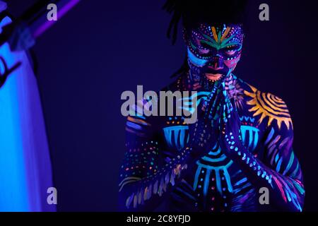 portrait of calm african man with fluorescent prints on skin praying for the best, stand in the pose of prayer. luminescence, fluorescence, body art c Stock Photo