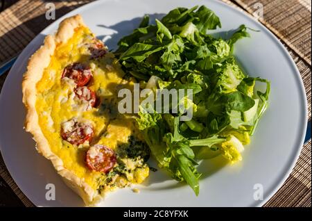 Outdoor table with Summer meal of tomato, spinach and egg pastry quiche lorraine and green salad Stock Photo