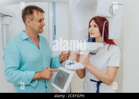 A woman patient makes a panoramic X-ray of the oral cavity using an orthopantomographic apparatus, and an assistant takes a picture Stock Photo