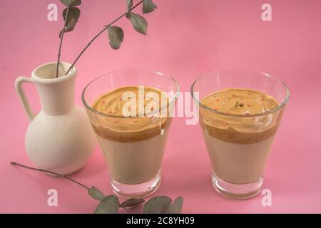 Two glasses of home made iced coffee with decorative white vase. Pink background
