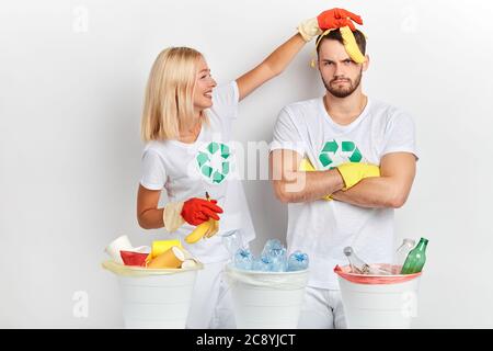 young funny blonde cheerful girl having fun with banana while sorting waste with her frustrated friend , close uop photo. entertainment . Stock Photo