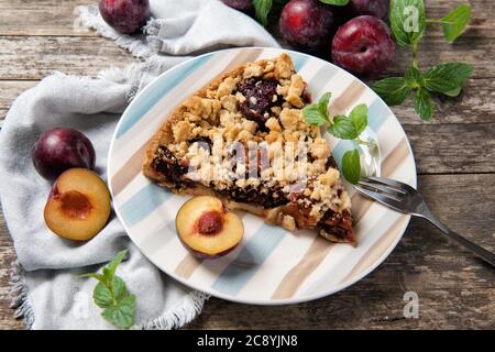 Piece of home made Plum Cake on a plate with ripe plums and mint leaves, wooden table Stock Photo