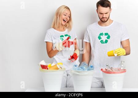 young happy woman in white t-shirt controlling how her boyfriend sorting waste, girl giving advice her man, recycling activity Stock Photo