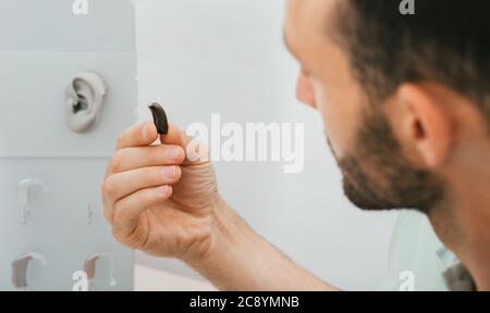 Hearing aid, a man holds a hearing solution close-up. A hearing-impaired middle-aged man with a hearing aid Stock Photo