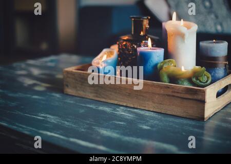 Various colored burning candles on wooden table in modern home, in wooden retro box, cozy style interior decoration Stock Photo