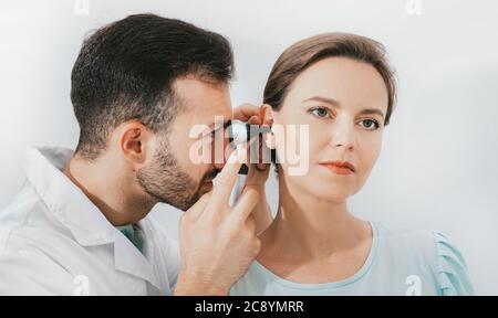 Woman patient getting ear exam at the clinic, experienced doctor examining woman ear, using an otoscope Stock Photo