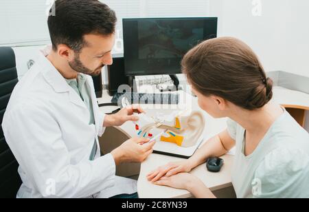 Mixed race audiologist showing beautiful woman patient an eardrum on model of human ear. Complaints of bed hearing in adults Stock Photo