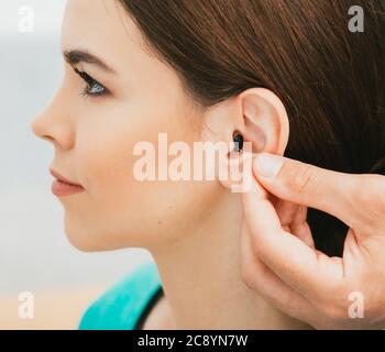 Young patient with Intra-ear hearing aid, close-up on female ear. The hearing solution, audiologist inserting hearing aid Stock Photo