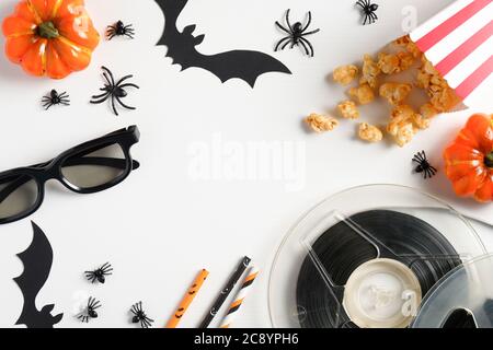 Halloween scary movie concept. Flat lay composition with popcorn, orange pumpkins, bobbins, glasses, halloween decorations on white table. Top view. Stock Photo