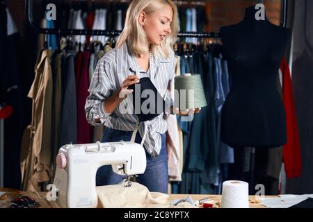 cute tailor holding tow big thread in hands matching them to sew. close up side view photo. sloution concept. lifestyle, free time Stock Photo