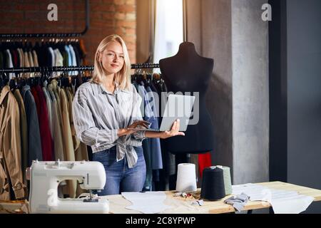 awesome young female dressmaker holding laptop, looking at the camera . close up photo. sewing, needlework online lesson, education Stock Photo
