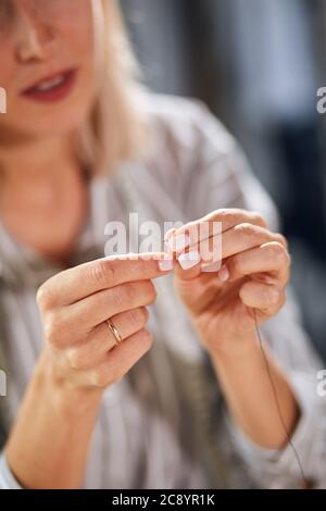 woman threading needle at home, focus on palms, hands. blurred background, sewing tool. equipment. close up cropped photo Stock Photo