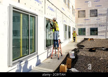 A glazier on a ladder, applying weather sealant around the edges of newly installed windows at a construction site. Stock Photo