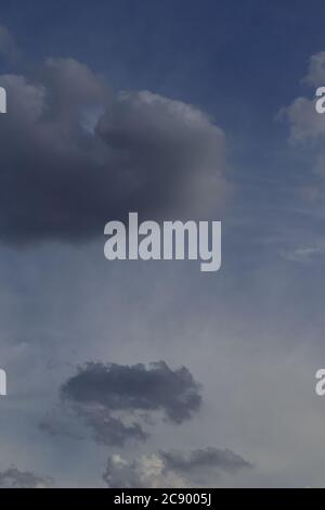 Fluffy shaded gray clouds floating under a misty blue sky. Stock Photo