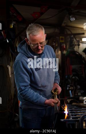The Blazing Blacksmith Jim Whitson working on a garden gate in his workshop at Waterheads near Eddleston Stock Photo