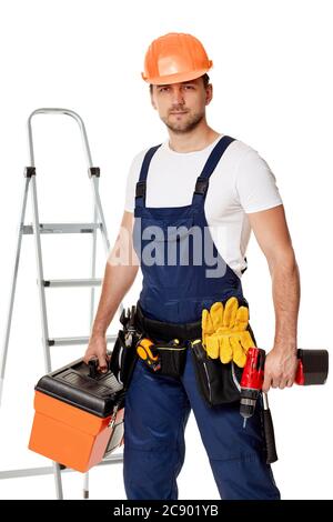 caucasian repairman worker in uniform and helmet holding cordless screwdriver and tool box. handyman wearing tool belt isolated on studio background Stock Photo