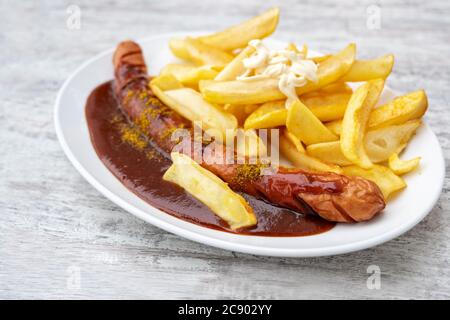Currywurst, sausage with curry ketchup, a popular fast food in Germany, served with French fries and mayonnaise on an oval plate on a grey background, Stock Photo