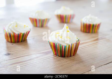 Cupcakes with lemon sprinkles in colorful cake tins, on a wooden table Stock Photo
