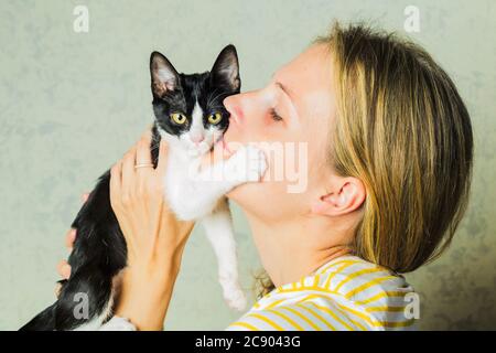 Life style photo of a casual dressed female who is holding and petting and kissing cute a  cat. cat enjoys being in girls arms. Selective focus. Stock Photo