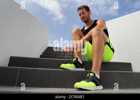 Runner tying running shoes laces getting ready to run on city stairs. Healthy active lifestyle man happy jogging motivation Stock Photo