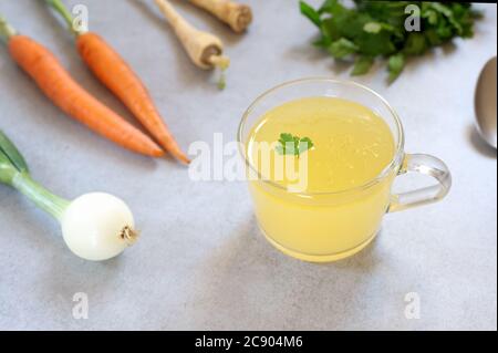 Bone broth, bone stock in a glass cup and vegetables  on the background.  Paleo diet.Horizontal,with selective focus. Stock Photo