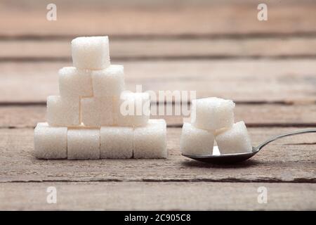 The refined sugar in cubes in a tea spoon on a wooden table from old boards. Stock Photo